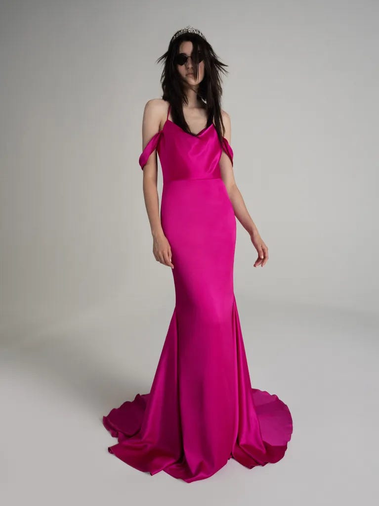 Brunette wearing sunglasses in a pink strapless mermaid party dress with draped neckline, against a grey background.